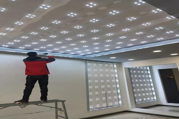 An installer laying out an LED grid and applying aluminum foil tape for a backlit stretch ceiling sky